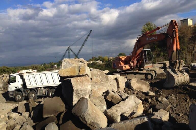 Escavatore e camion in un cantiere con rocce.