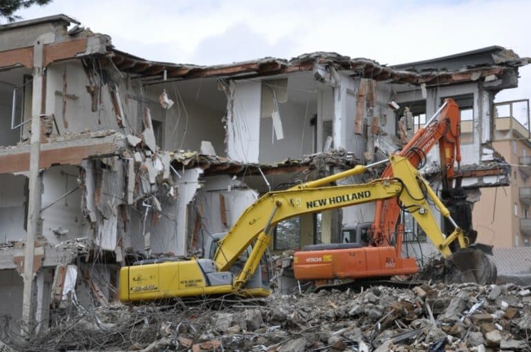 Escavatrici demoliscono un edificio parzialmente distrutto.