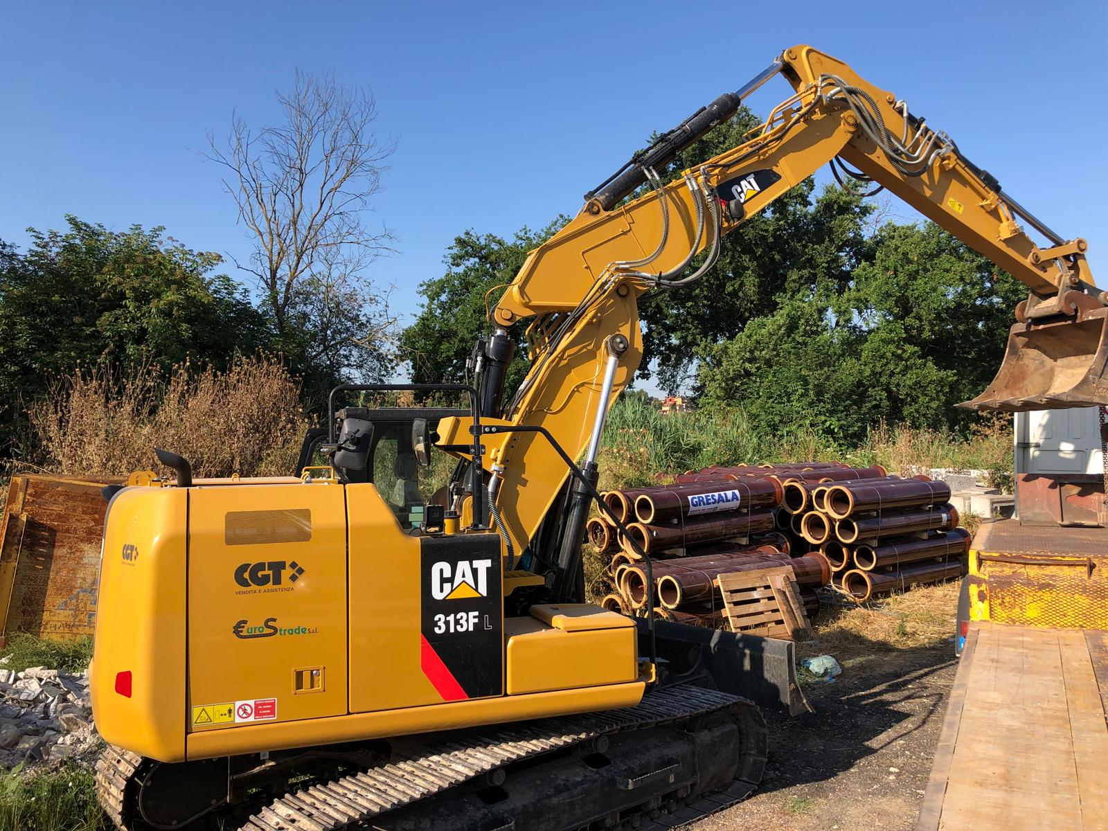 Escavatore giallo su un cantiere con tubi accatastati.
