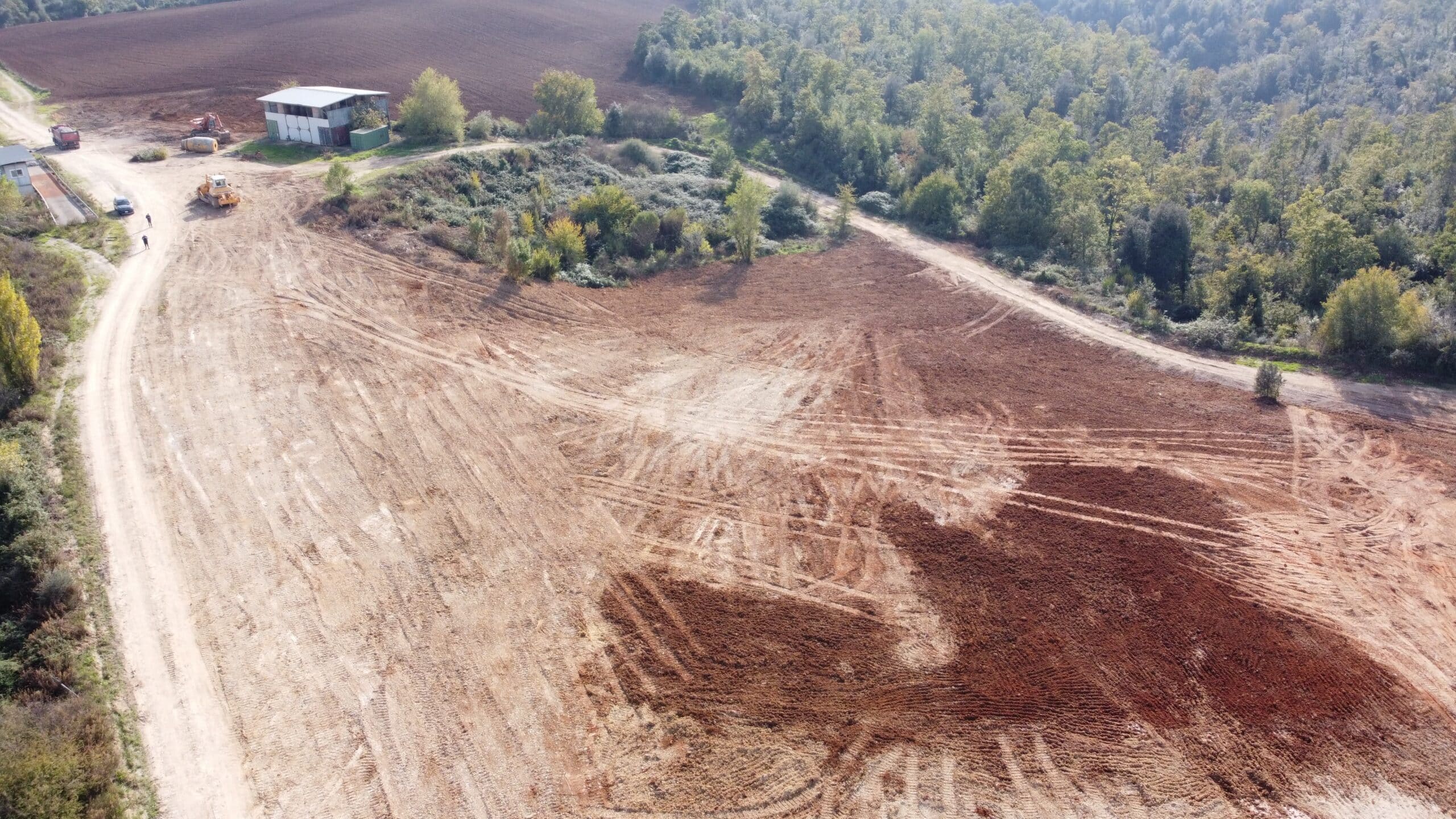 Terreno spianato con macchinari e vegetazione circostante.