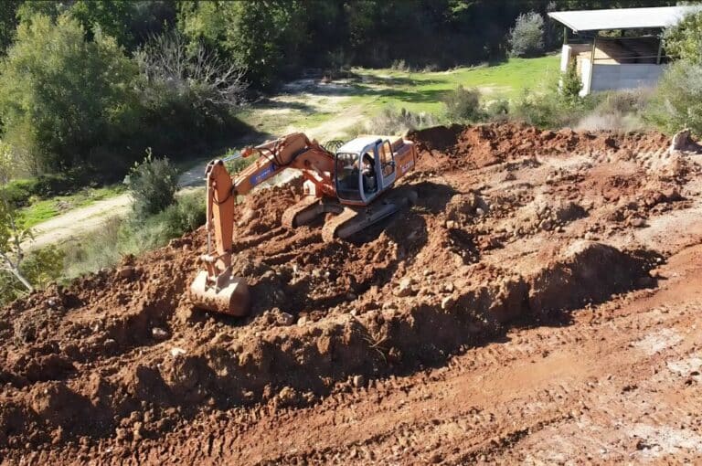 Escavatore in azione su terreno fangoso, circondato da alberi.