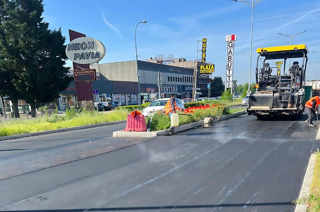 Operai asfaltano strada vicino a edifici commerciali.